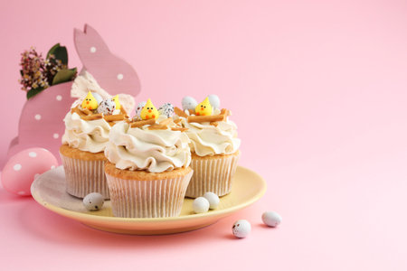 Tasty Easter cupcakes with vanilla cream and candies on pink background, space for textの写真素材