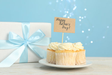 Happy Father's Day. Tasty cupcakes with greetings and gift box on light wooden table, closeupの写真素材