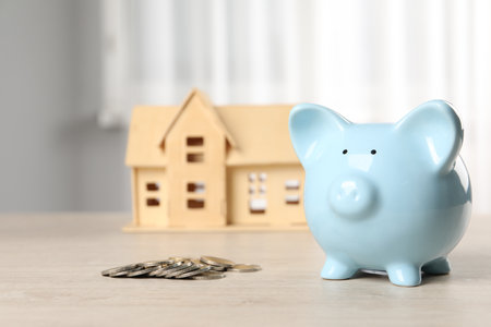 House model, piggy bank and coins on wooden table indoors, selective focusの写真素材