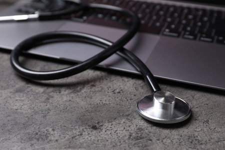 Laptop and stethoscope on gray table, closeup