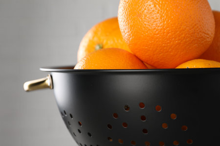 Fresh ripe oranges in black colander on light background, closeup