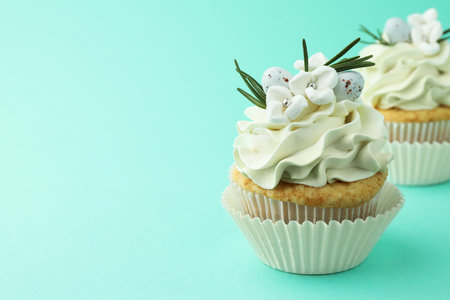 Tasty Easter cupcakes with vanilla cream on turquoise background, space for text