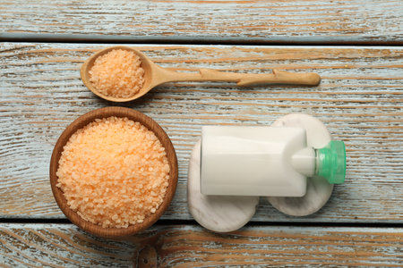 Orange sea salt in bowl, spa stones, cosmetic product and spoon on wooden table, flat lay
