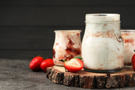 Tasty yoghurt with jam and strawberries on gray textured table, closeup. Space for textの写真素材