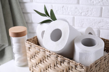 Toilet paper rolls in wicker basket, floral decor and cotton pads on tableの写真素材