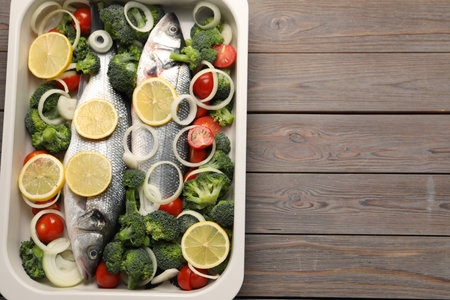 Raw fish with vegetables and lemon in baking dish on wooden table, top view. Space for textの写真素材