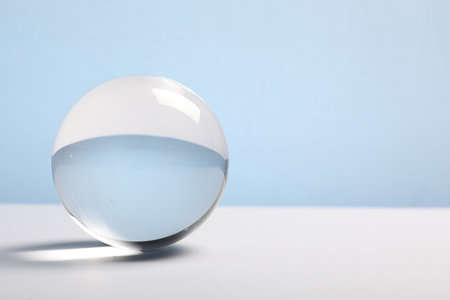 Transparent glass ball on table against light blue background. Space for textの写真素材