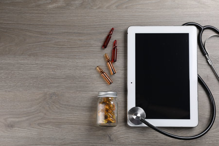 Modern tablet, stethoscope, ampoules and bottle with pills on wooden table, flat lay. Space for textの写真素材