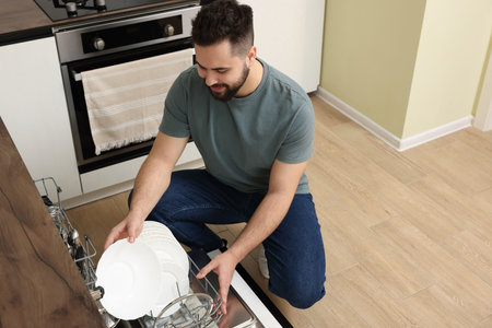 Smiling man loading dishwasher with plates in kitchen. Space for textの写真素材