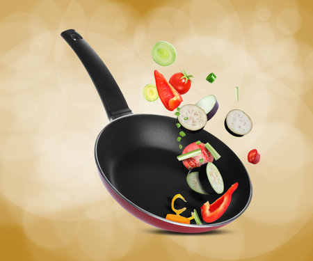 Frying pan with fresh ingredients in air on color backgroundの写真素材
