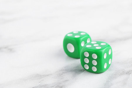 Two green game dices on white marble table, closeup