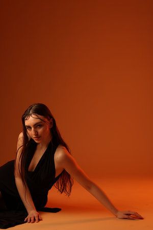 Beautiful woman in black dress posing on brown background. Space for textの写真素材