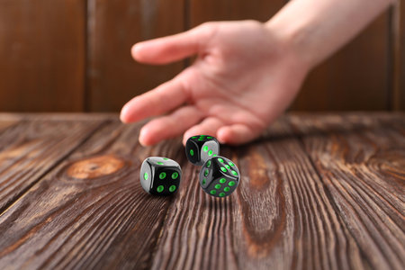 Woman throwing black dice on wooden table, closeupの写真素材