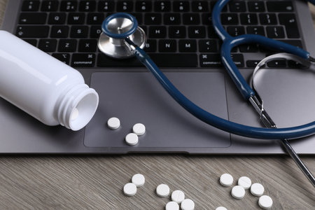 Laptop, stethoscope, pills and bottle on wooden table, closeupの写真素材