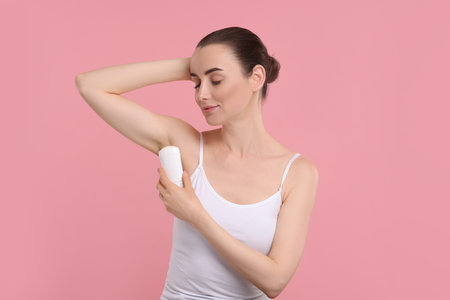 Beautiful woman applying deodorant on pink backgroundの写真素材