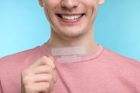 Young man with whitening strips on light blue background, closeupの写真素材