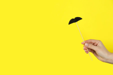 Woman with fake paper mustache on yellow background, closeup. Space for textの写真素材