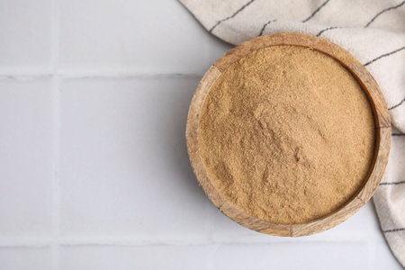 Dietary fiber. Psyllium husk powder in bowl on white tiled table, top view. Space for text
