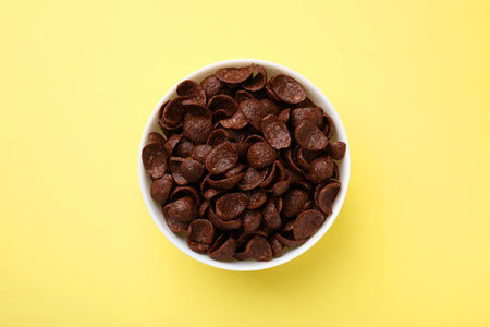 Breakfast cereal. Chocolate corn flakes in bowl on yellow table, top view