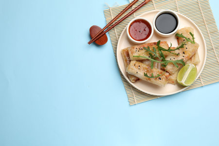 Tasty fried spring rolls served on light blue table, flat lay. Space for textの写真素材