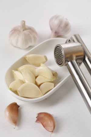 Metal press and garlic on white wooden table, closeupの写真素材