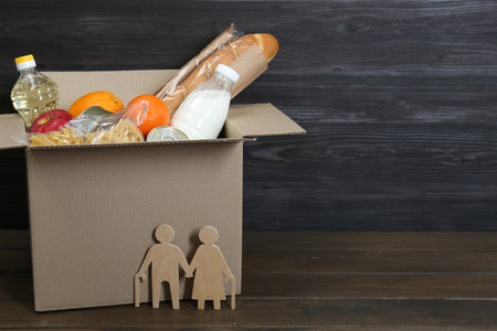 Humanitarian aid for elderly people. Cardboard box with food donation and figures of couple on...