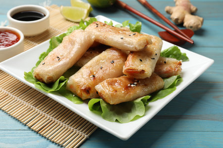 Tasty fried spring rolls and lettuce on light blue wooden table, closeup