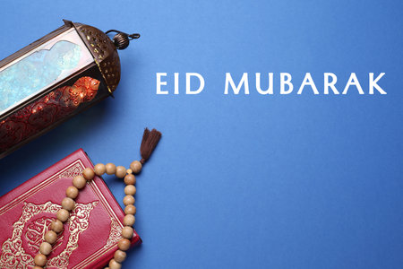 Eid Mubarak greeting card. Arabic lantern, Quran and misbaha on blue background, flat layの写真素材