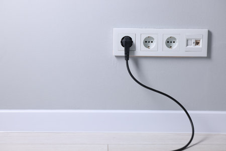 Power sockets and electric plug on gray wall, space for text