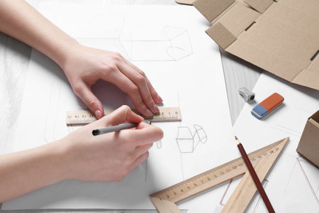 Woman creating packaging design at light wooden table, closeup