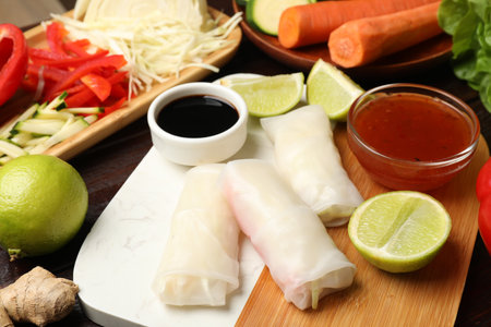 Delicious spring rolls with vegetables, lime and sauces on table, closeup