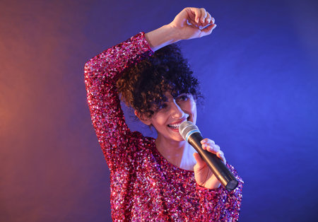 Beautiful young woman with microphone singing on color background in neon lights