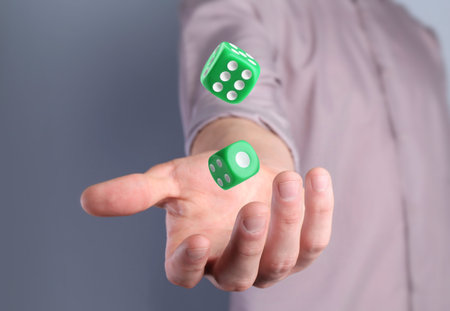 Man throwing green dice on gray background, closeup