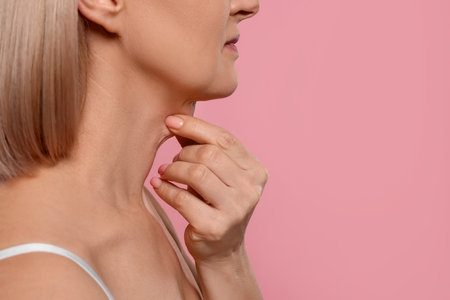 Woman touching her neck on pink background, closeup. Space for textの写真素材