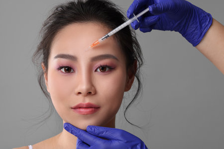 Woman getting facial injection on grey background