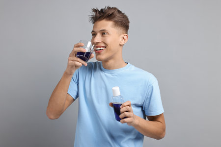 Young man using mouthwash on light grey background