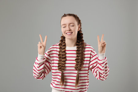 Woman with braided hair showing peace sign on grey backgroundの写真素材