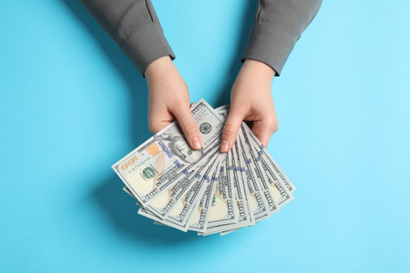 Money exchange. Woman holding dollar banknotes on light blue background, top viewの写真素材