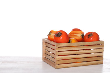 Delicious ripe juicy persimmons in crate on wooden table against white backgroundの写真素材