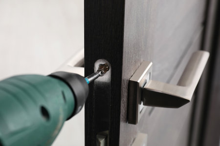 Repairing door handle with electric screwdriver indoors, closeup
