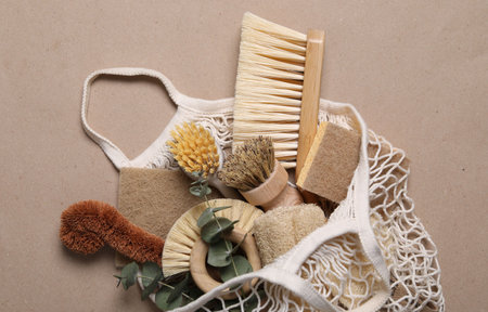 Cleaning brushes, sponges, eucalyptus leaves and string bag on pale brown background, top viewの写真素材