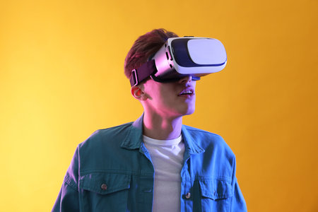 Young man with virtual reality headset on yellow background