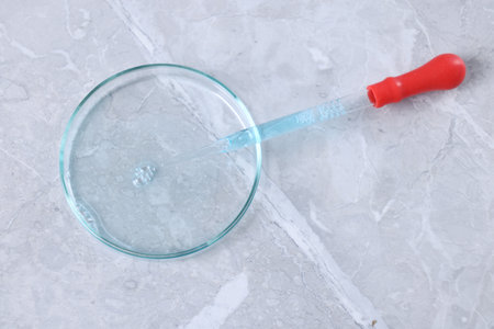 Glass pipette and petri dish with liquid on gray marble table, top view