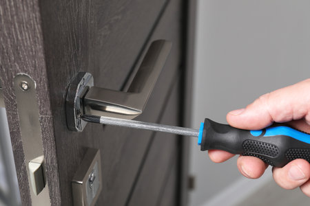 Handyman with screwdriver repairing door handle indoors, closeup