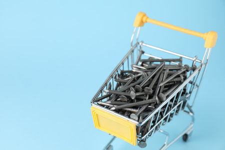 Metal nails in shopping cart on light blue background, closeup. Space for textの写真素材