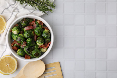 Delicious roasted Brussels sprouts and bacon served on white tiled table, flat lay. Space for textの写真素材