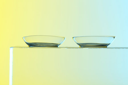 Pair of contact lenses on glass against light background, closeup