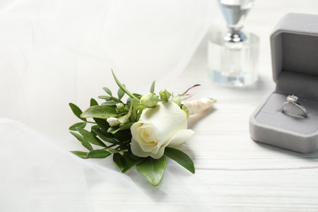 Wedding stuff. Stylish boutonniere, perfume and ring on white wooden table, closeup