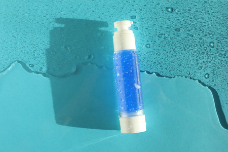 Bottle of cosmetic product in water on turquoise background, top view