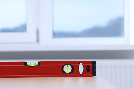 Red building level on wooden table indoors, closeup. Space for text